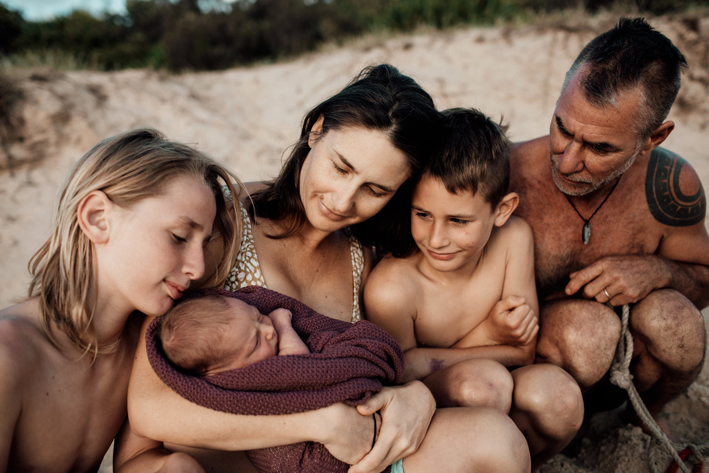 Family gathered around a sleeping newborn at the beach