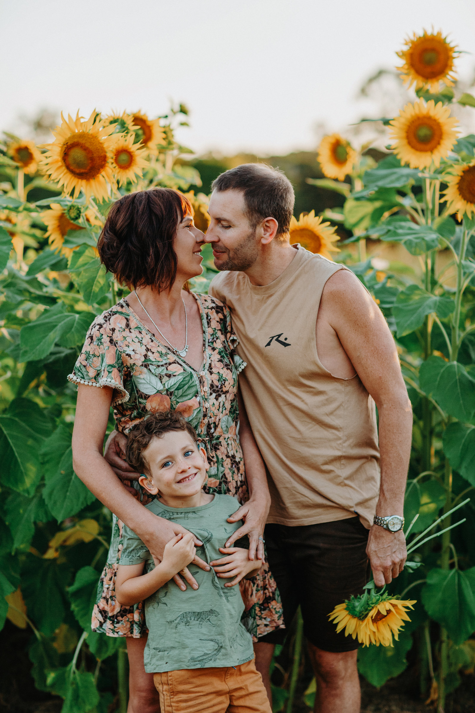 Two adults and a child standing together in a sunflower field
