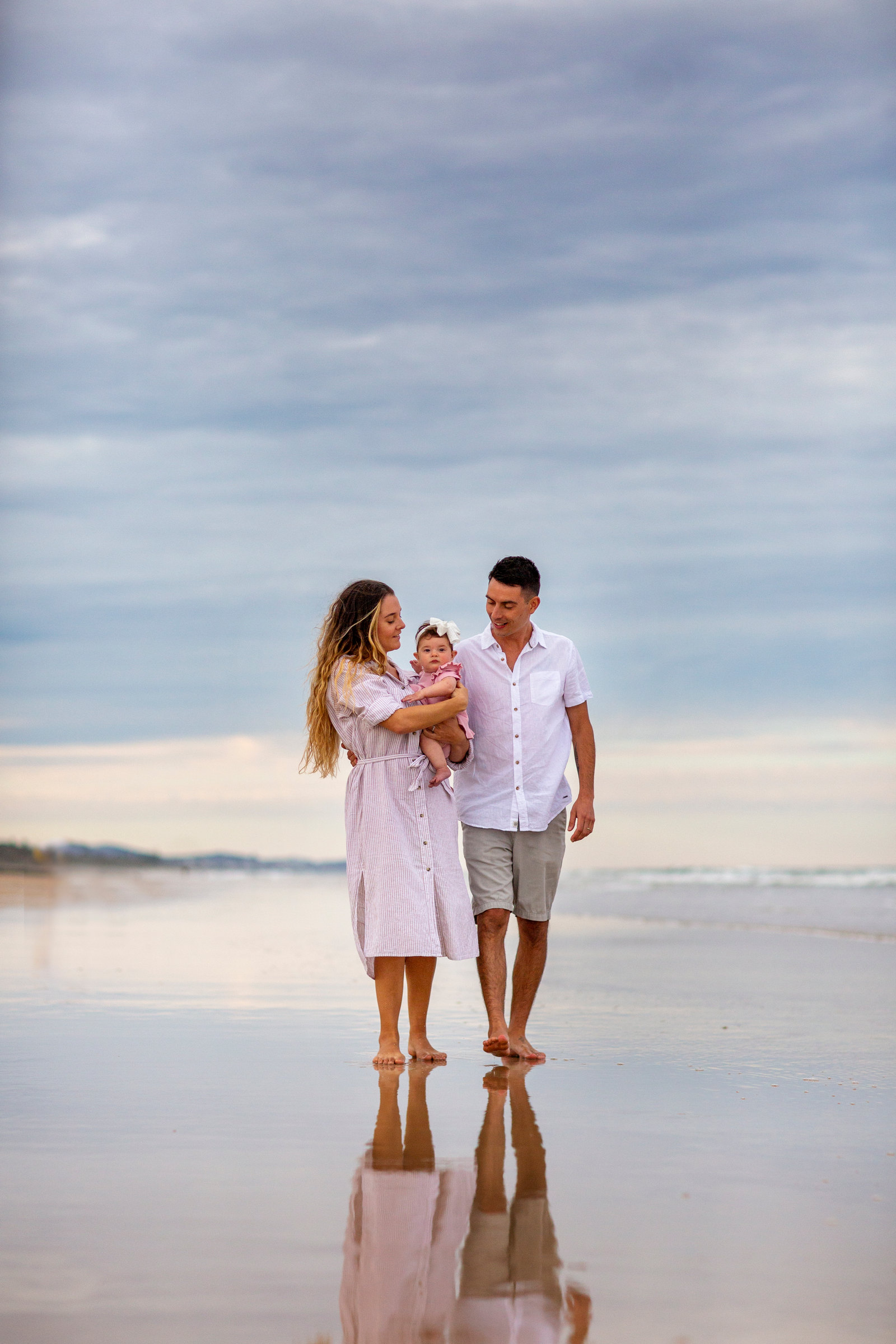 Two adults walking with a baby on a reflective beach